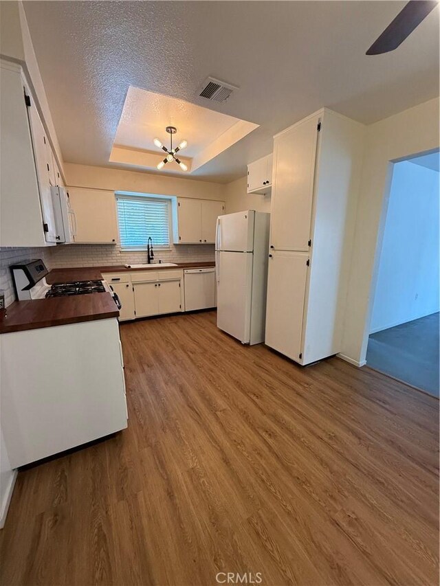 749 Junipero Ct, Merced, CA 95348 - kitchen featuring visible vents, wood finished floors, white cabinets, a tray ceiling, and white appliances