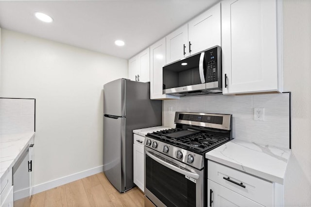 kitchen with light hardwood / wood-style floors, appliances with stainless steel finishes, white cabinetry, and light stone countertops