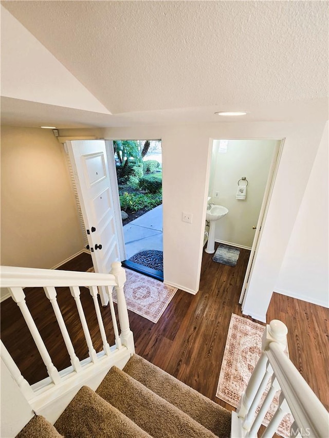 foyer featuring a textured ceiling, dark wood-style flooring, baseboards, vaulted ceiling, and stairway