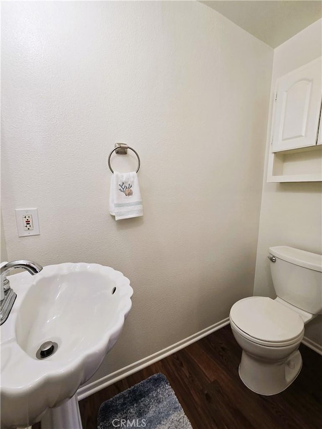 half bathroom featuring a sink, baseboards, toilet, and wood finished floors