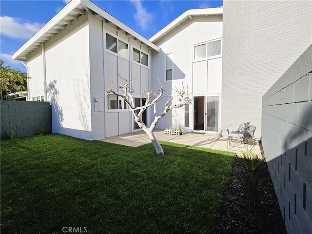 back of property with a yard, fence, stucco siding, and a patio