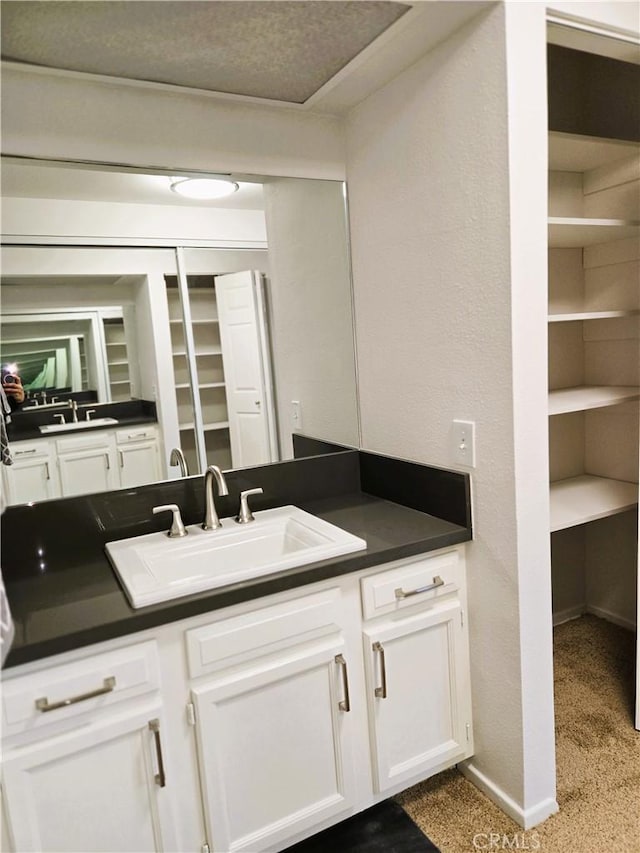 kitchen with dark countertops, white cabinetry, a sink, and baseboards