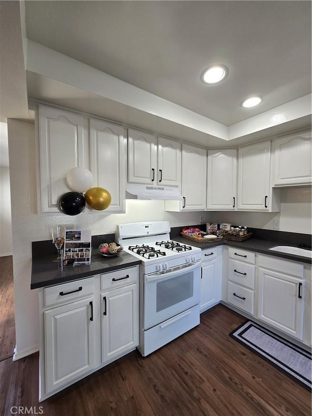 kitchen with dark countertops, white cabinets, white gas stove, and under cabinet range hood