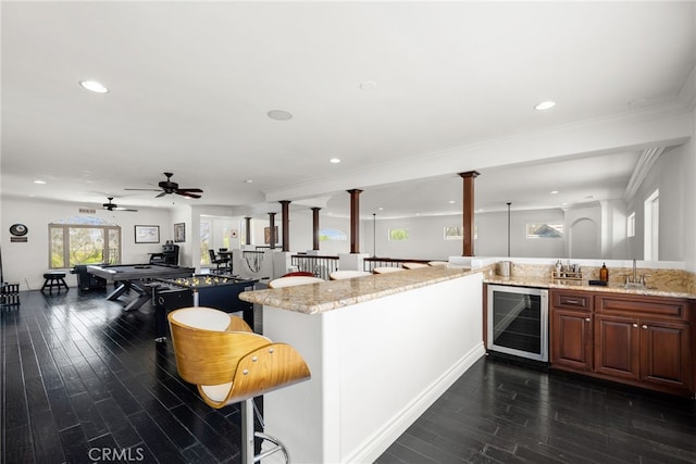 kitchen with light stone countertops, a breakfast bar, beverage cooler, decorative columns, and kitchen peninsula