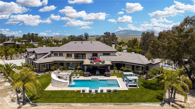 rear view of property with a mountain view, pool water feature, a yard, and a patio