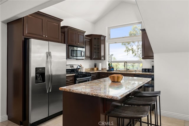 kitchen with stainless steel appliances, a breakfast bar, a center island, light stone countertops, and sink