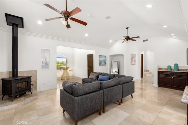 living room with ceiling fan, ornamental molding, a wood stove, and lofted ceiling