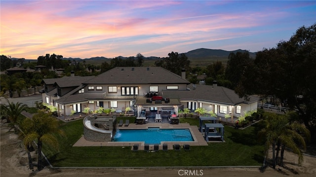 back house at dusk featuring a mountain view, a patio, pool water feature, and a yard