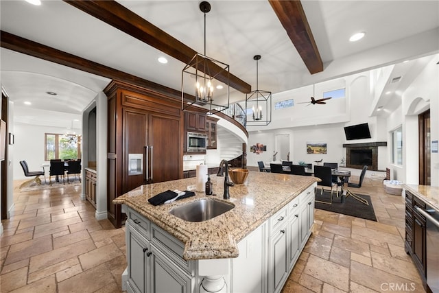 kitchen with sink, stainless steel microwave, hanging light fixtures, an island with sink, and beam ceiling