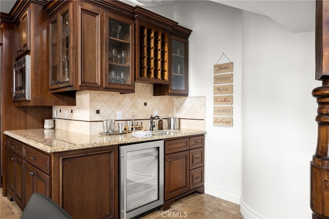 bar featuring light stone counters, stainless steel microwave, wine cooler, dark brown cabinetry, and tasteful backsplash