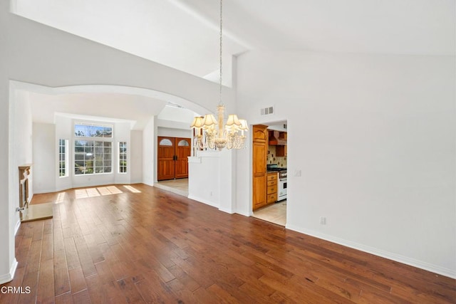 unfurnished living room featuring arched walkways, visible vents, light wood-style floors, a chandelier, and baseboards