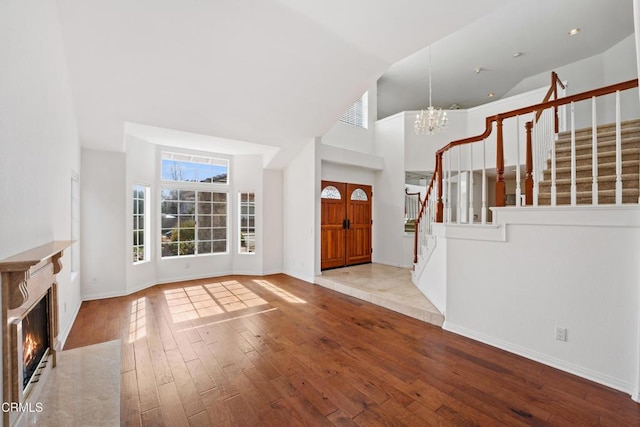 entryway with high vaulted ceiling, stairway, light wood-type flooring, a glass covered fireplace, and an inviting chandelier