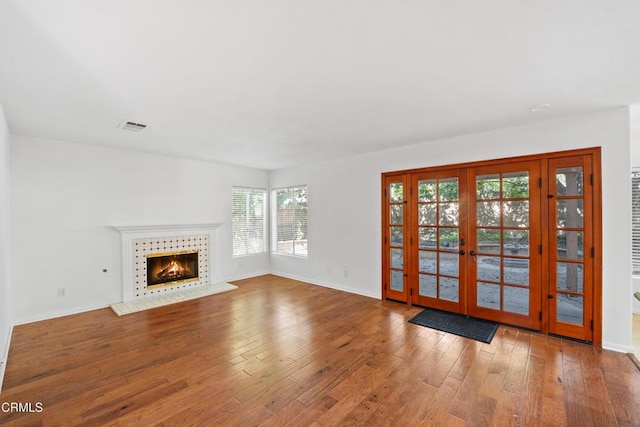 unfurnished living room with baseboards, visible vents, a tiled fireplace, light wood-style flooring, and french doors