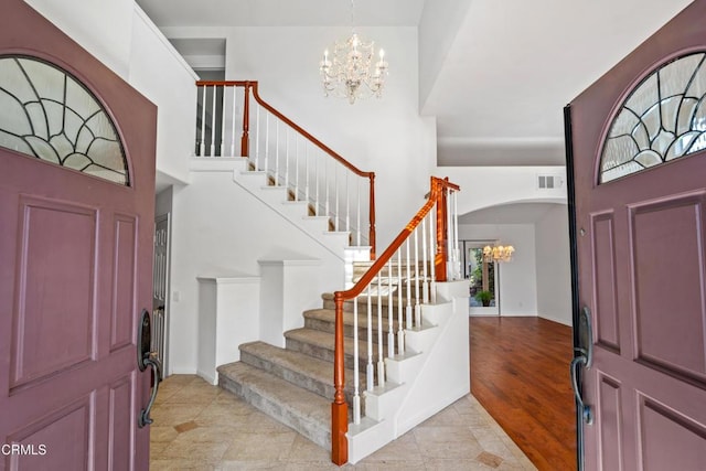 foyer with stairway, a towering ceiling, visible vents, and an inviting chandelier