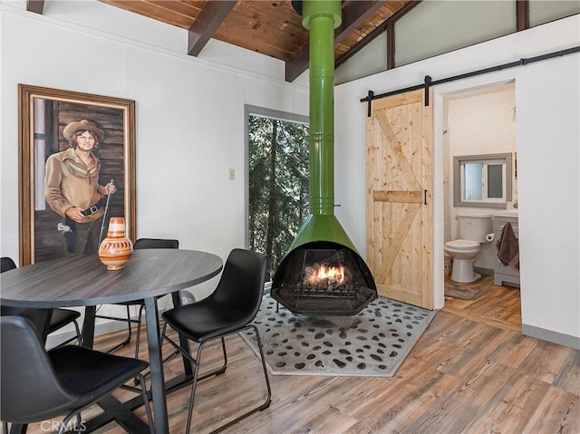 dining room with lofted ceiling with beams, a wood stove, a barn door, wood finished floors, and wood ceiling