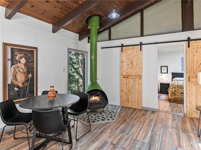 dining room featuring wood finished floors, wooden ceiling, a barn door, vaulted ceiling with beams, and a wood stove