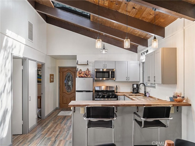 kitchen featuring a kitchen breakfast bar, appliances with stainless steel finishes, wood counters, hanging light fixtures, and a sink