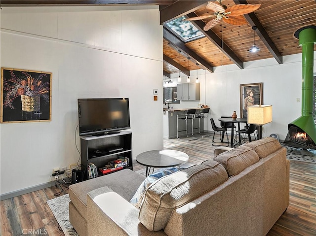 living area featuring lofted ceiling with skylight, wood finished floors, a ceiling fan, a wood stove, and wood ceiling