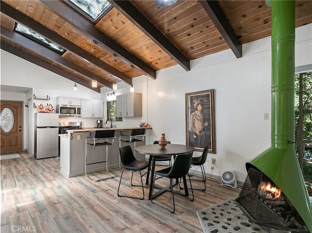 dining space with a wealth of natural light, lofted ceiling with skylight, light wood-style floors, and a wood stove