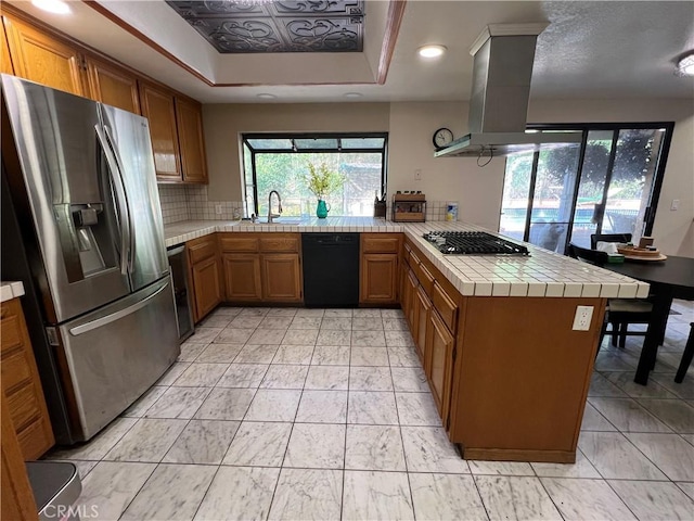 kitchen with stainless steel appliances, island exhaust hood, a tray ceiling, sink, and kitchen peninsula