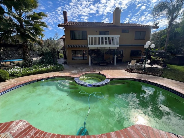 rear view of property featuring a patio area, an in ground hot tub, and a balcony