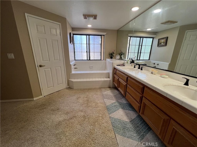 bathroom featuring a healthy amount of sunlight, vanity, and a relaxing tiled tub