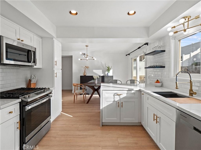 kitchen with white cabinetry, sink, stainless steel appliances, and hanging light fixtures