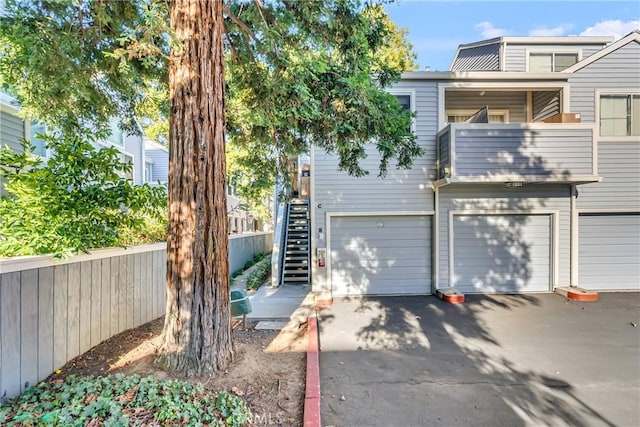 exterior space with stairway, an attached garage, a balcony, and aphalt driveway