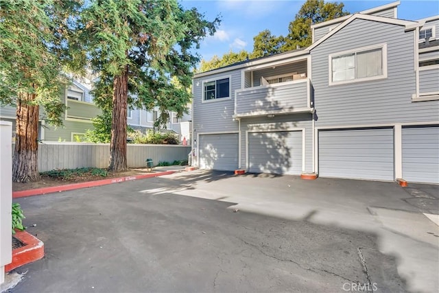 view of front of house with a garage, driveway, a balcony, and fence