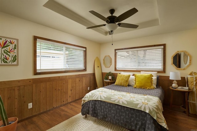 bedroom with a raised ceiling, ceiling fan, wooden walls, and dark hardwood / wood-style flooring