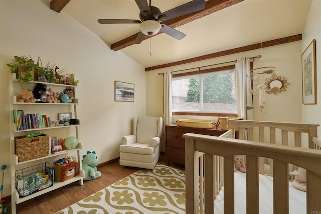 bedroom featuring a crib, ceiling fan, hardwood / wood-style flooring, and vaulted ceiling with beams