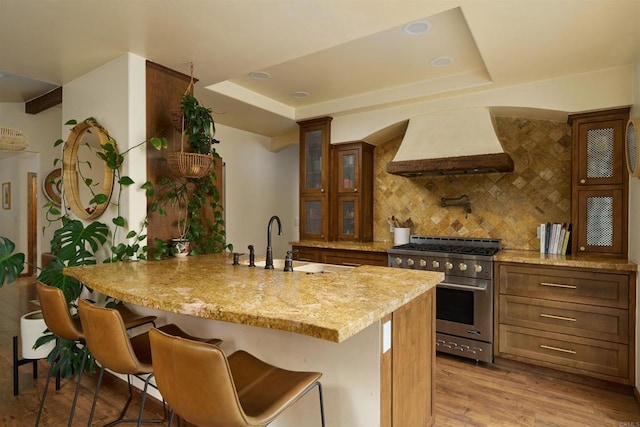 kitchen featuring an island with sink, a breakfast bar, high end stainless steel range oven, sink, and custom exhaust hood