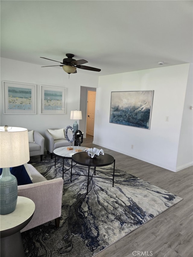 living area with baseboards, a ceiling fan, and wood finished floors