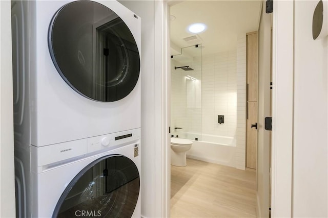 laundry area with stacked washing maching and dryer, wood finished floors, visible vents, and laundry area