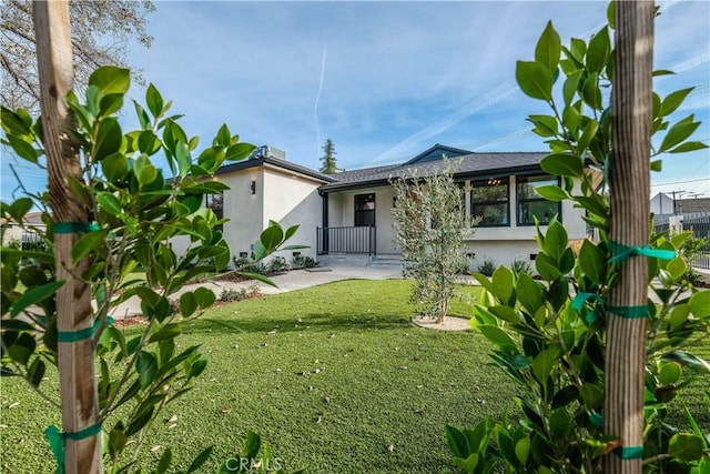 rear view of property with a patio area, a yard, fence, and stucco siding