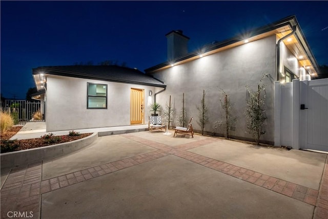 18848 Collins St, Tarzana, CA 91356 - back of house at twilight featuring stucco siding, a chimney, a patio, fence, and a gate
