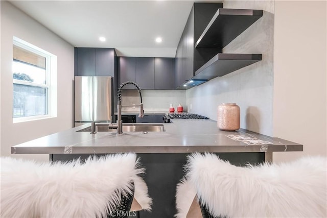 kitchen featuring wall chimney range hood, modern cabinets, a sink, freestanding refrigerator, and a peninsula