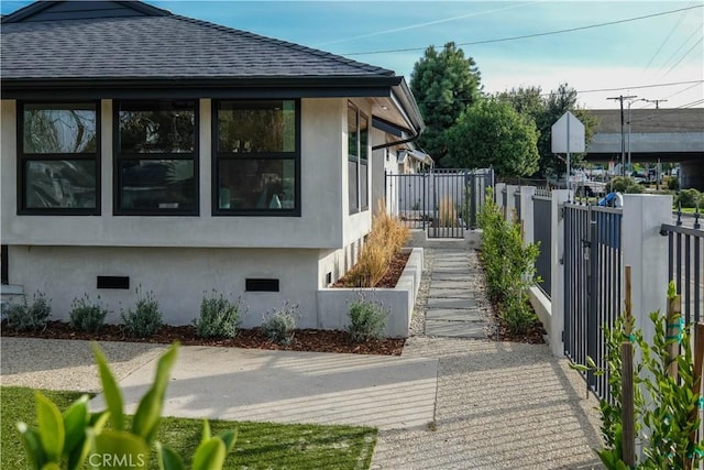 view of home's exterior featuring a fenced front yard, roof with shingles, and stucco siding