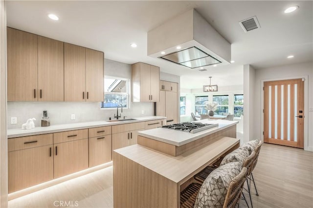 kitchen with a center island, stainless steel gas cooktop, light countertops, visible vents, and a sink