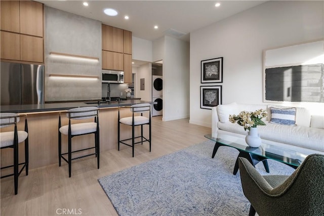 living room with visible vents, baseboards, stacked washing maching and dryer, recessed lighting, and light wood finished floors