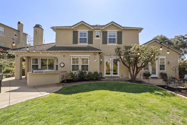 traditional home with french doors, stucco siding, an outdoor kitchen, a patio area, and a front lawn