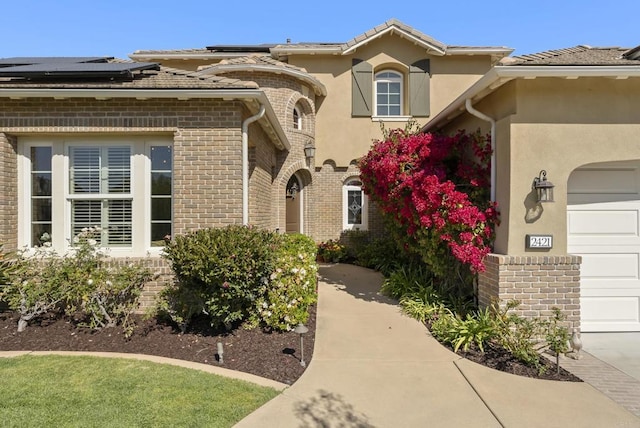 view of front of property featuring stucco siding, brick siding, an attached garage, and solar panels