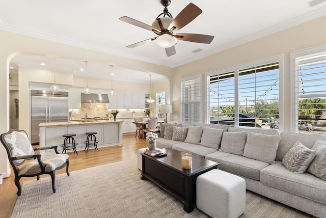 living room featuring ceiling fan, light wood finished floors, a wealth of natural light, and crown molding