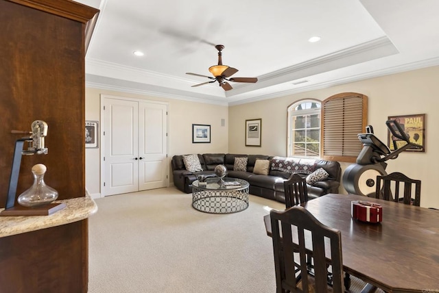 living room with a ceiling fan, a tray ceiling, light carpet, and crown molding