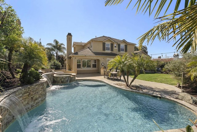 back of house with a patio area, a pool with connected hot tub, a chimney, and stucco siding