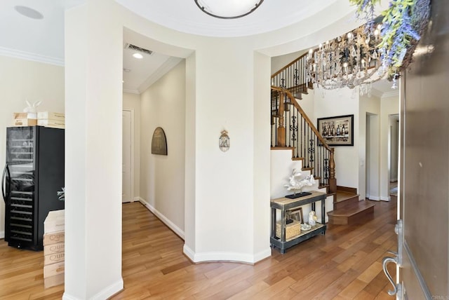 entryway with wine cooler, visible vents, ornamental molding, stairway, and light wood-type flooring