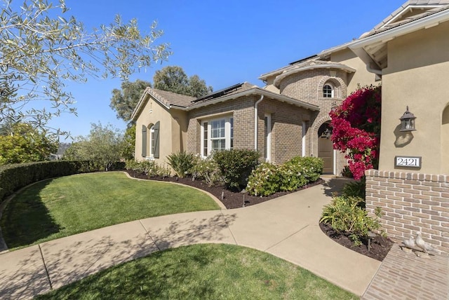 view of home's exterior with roof mounted solar panels, brick siding, a yard, and stucco siding