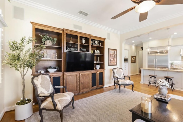 living room with visible vents, arched walkways, a ceiling fan, light wood-style flooring, and crown molding