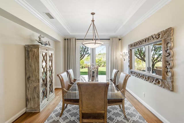 dining space with visible vents, baseboards, light wood-type flooring, a tray ceiling, and crown molding