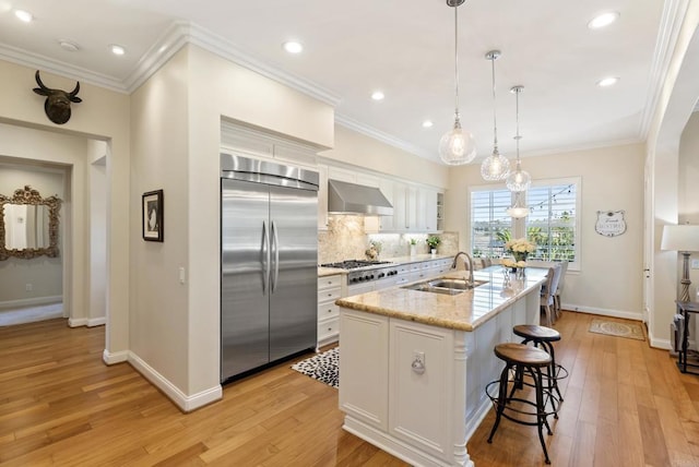 kitchen with stainless steel appliances, a sink, white cabinetry, wall chimney exhaust hood, and crown molding